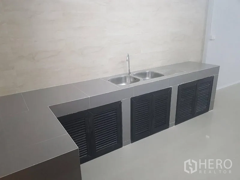 Shophouse for rent or sale in Lat Phrao, Bangkok - Long tiled kitchen counter with double sink and black louvered cabinet doors.