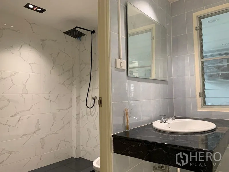 Townhouse for rent in Din Daeng, Bangkok - Bathroom with black stone vanity, mirror and rain shower enclosure.