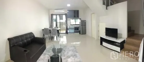Townhouse for rent or sale in Prawet, Bangkok - Bright open-plan living, dining and kitchen area with sofa, TV, dining set and staircase.