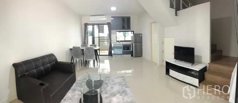 Townhouse for rent or sale in Prawet, Bangkok - Bright open-plan living, dining and kitchen area with sofa, TV, dining set and staircase.