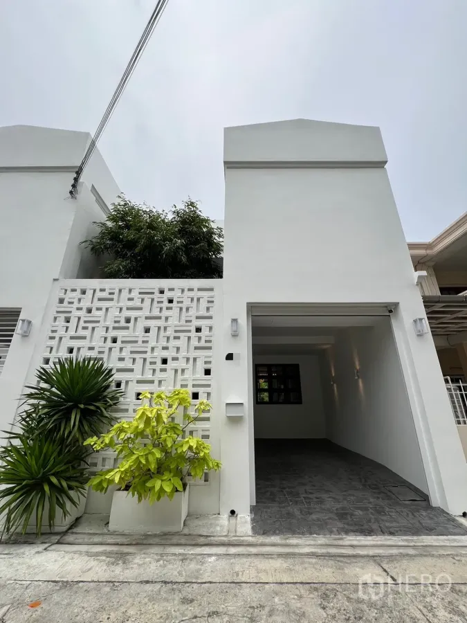 Townhouse for sale in Watthana, Bangkok - Freshly renovated white two-storey townhouse facade with breeze-block screen, potted plants and a covered carport.