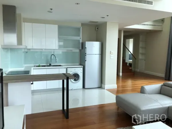 Condominium for rent or sale in Khlong Toei, Bangkok - Built-in white kitchen with fridge, washing machine and slim breakfast bar beside a staircase.