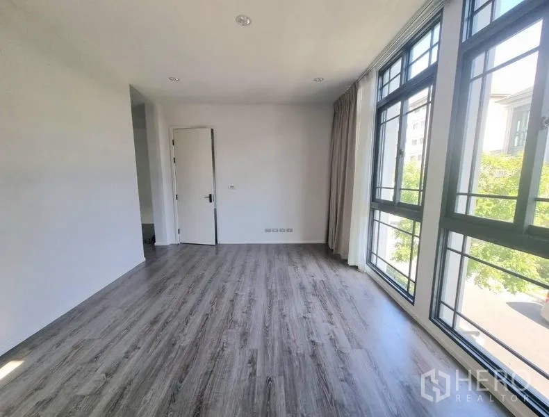 Detached House for rent - Sunlit bedroom with wall-length black-framed windows and grey wood floors.