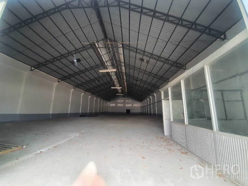 Warehouse for rent in Nakhon Pathom - Deep warehouse bay with steel roof structure and a partial glass partition wall.