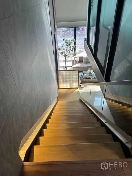 Home Office for rent in Bueng Kum, Bangkok - Wood staircase with glass railing overlooking a double-height lobby with tall windows.