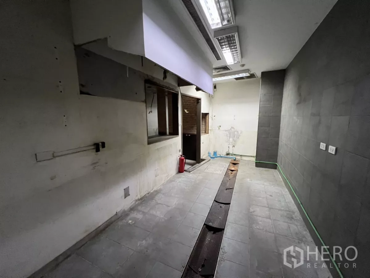 Retail Space for rent - Back-of-house prep room with tiled floor, fluorescent lights and a service opening.