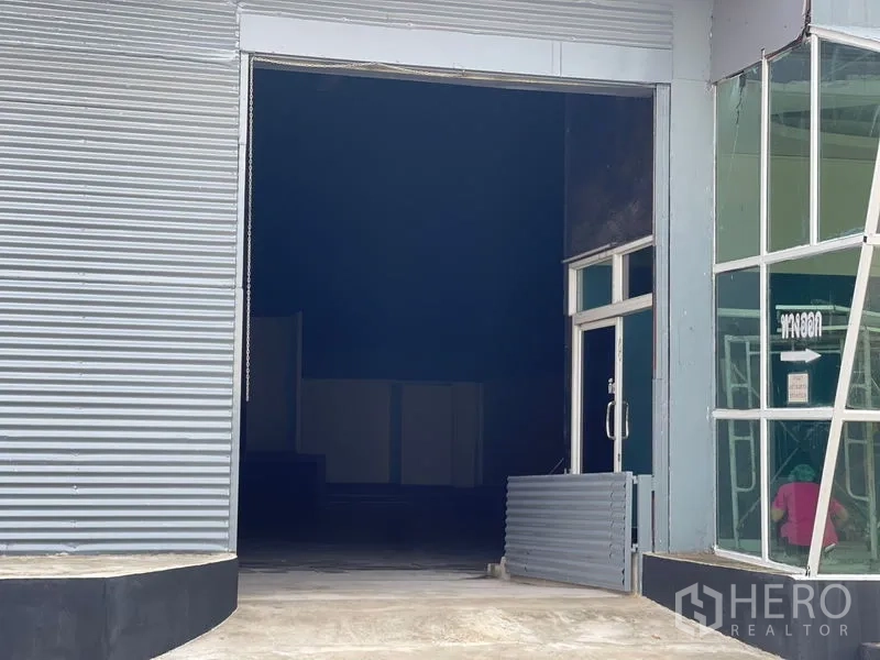 Warehouse for rent in Sam Phran, Nakhon Pathom - Loading bay view showing a large roller shutter and adjacent glass side door.
