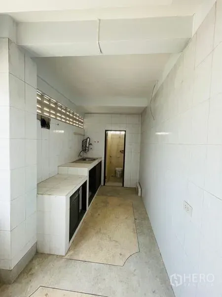 Shophouse for rent in Huai Khwang, Bangkok - Long tiled utility area with sink and access to a restroom.