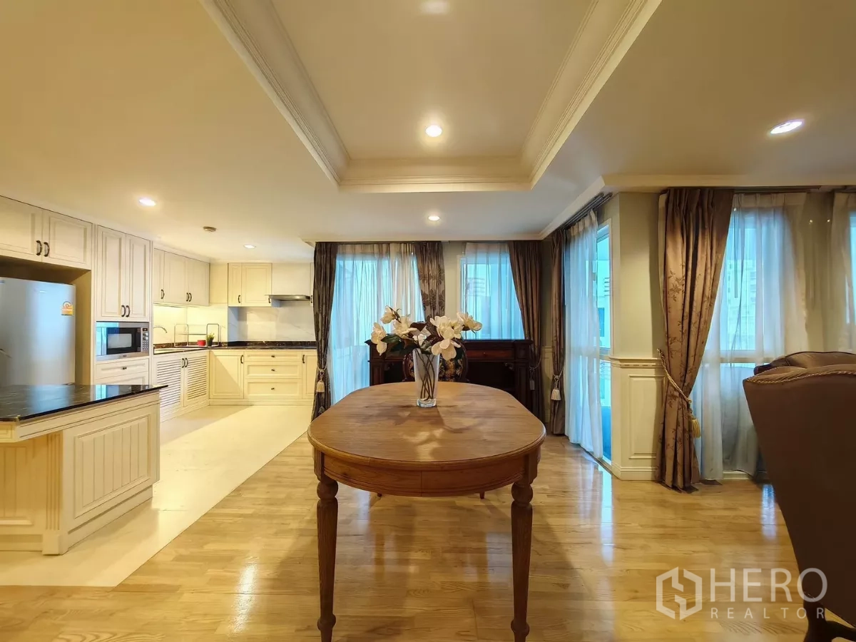Condominium for rent in Pathum Wan, Bangkok - Dining table facing an open U-shaped kitchen with cream cabinets and large windows.