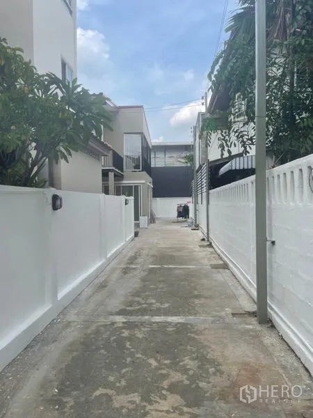 独立式住宅 出租在Huai Khwang, Bangkok - 通往住宅的私密小巷，白色围墙与路侧停车位。