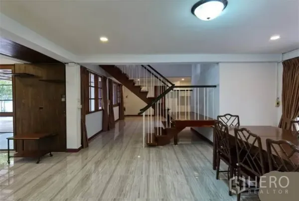 Detached House for rent in Watthana, Bangkok - Open-plan living and dining area with glossy tile floors and a wooden staircase.
