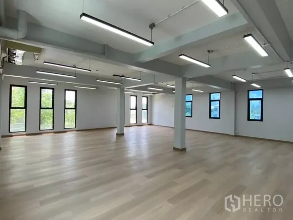 Home Office for rent in Phra Khanong, Bangkok - Large open office floor with light wood flooring, rows of LED strip lights, exposed services and tall windows for natural light.
