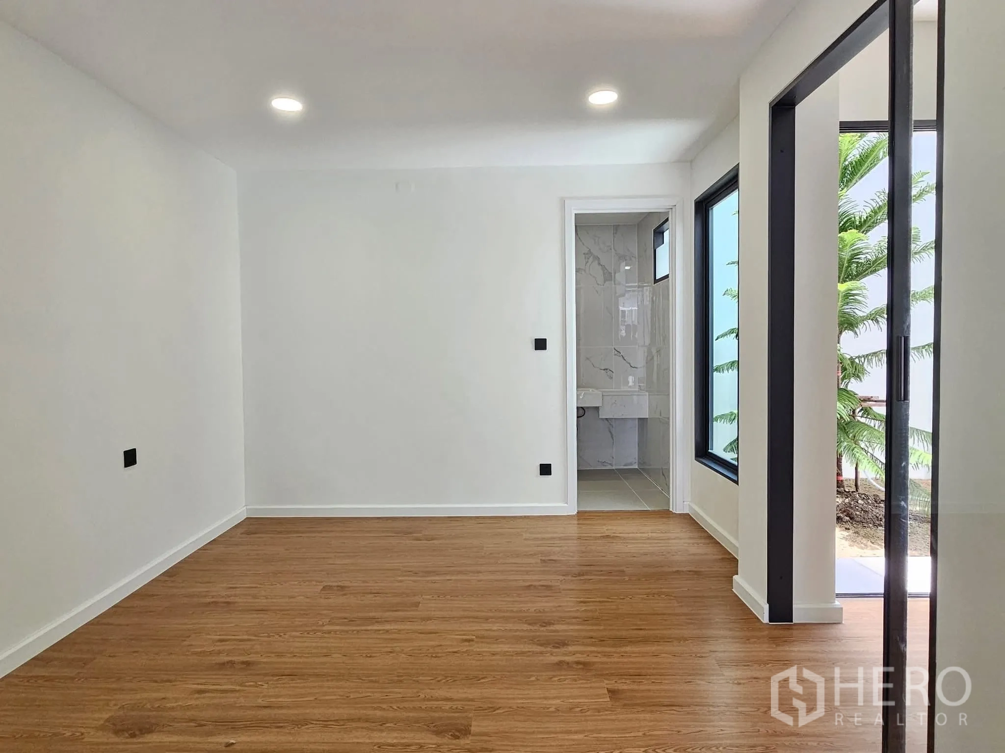 Detached House for sale in Lat Phrao, Bangkok - Ground-floor room with wood-style flooring, bathroom access, and windows looking to the garden.