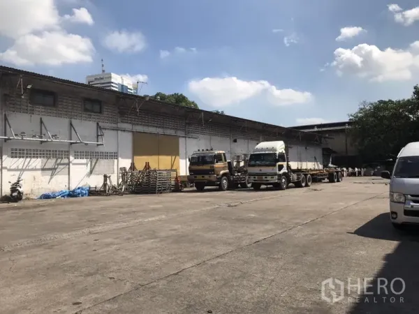 Warehouse for rent in Khlong Toei, Bangkok - Wide concrete yard with trucks in front of a long single‑storey warehouse with loading canopies.