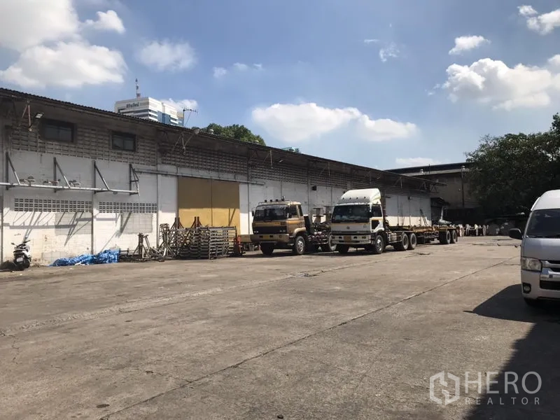 Warehouse for rent in Khlong Toei, Bangkok - Wide concrete yard with trucks in front of a long single‑storey warehouse with loading canopies.