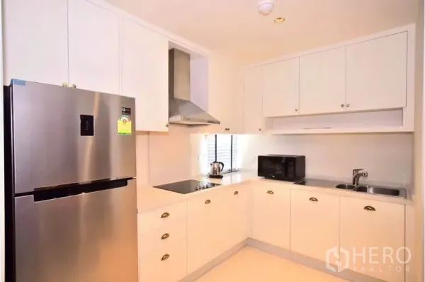Condominium for rent or sale in Khlong Toei, Bangkok - Bright U-shaped white kitchen with stainless-steel fridge, hob, hood and window lighting.