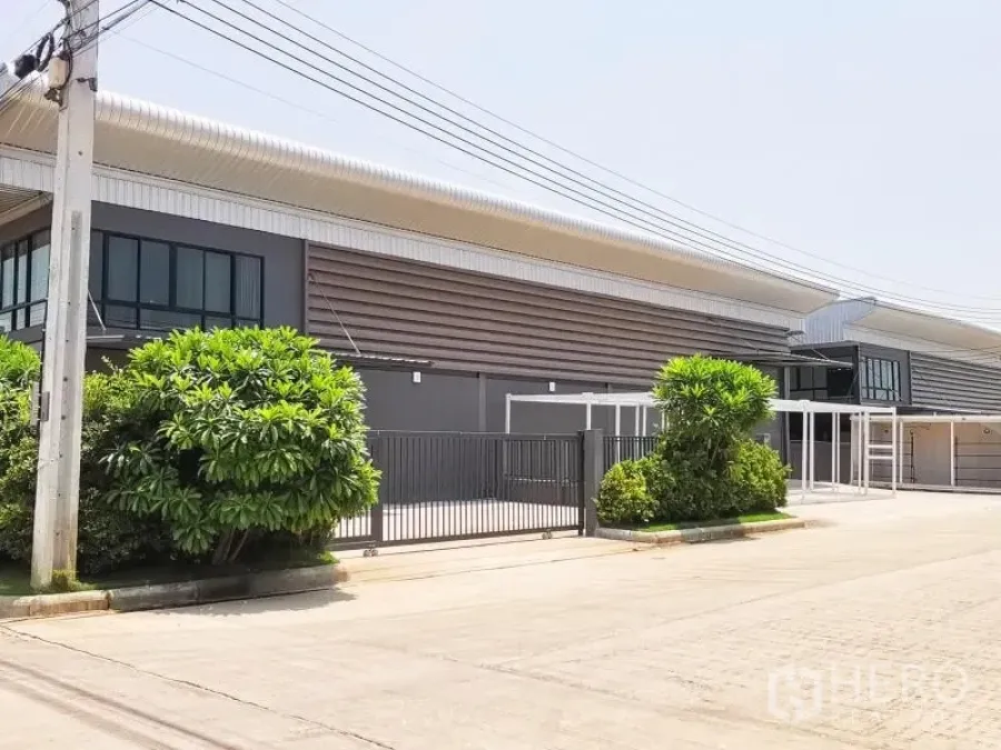 工厂 出租或出售在Bang Bo, Samut Prakan - 带大门的工业园区街景，绿化带与大跨度屋顶。