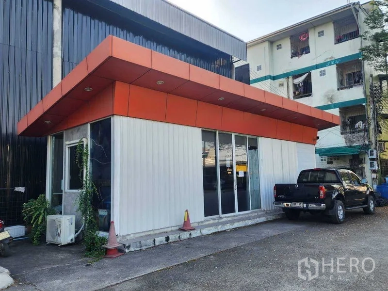 Warehouse for rent in Lat Phrao, Bangkok - Angled exterior of the office annex beside the warehouse with sliding glass doors and parking area.