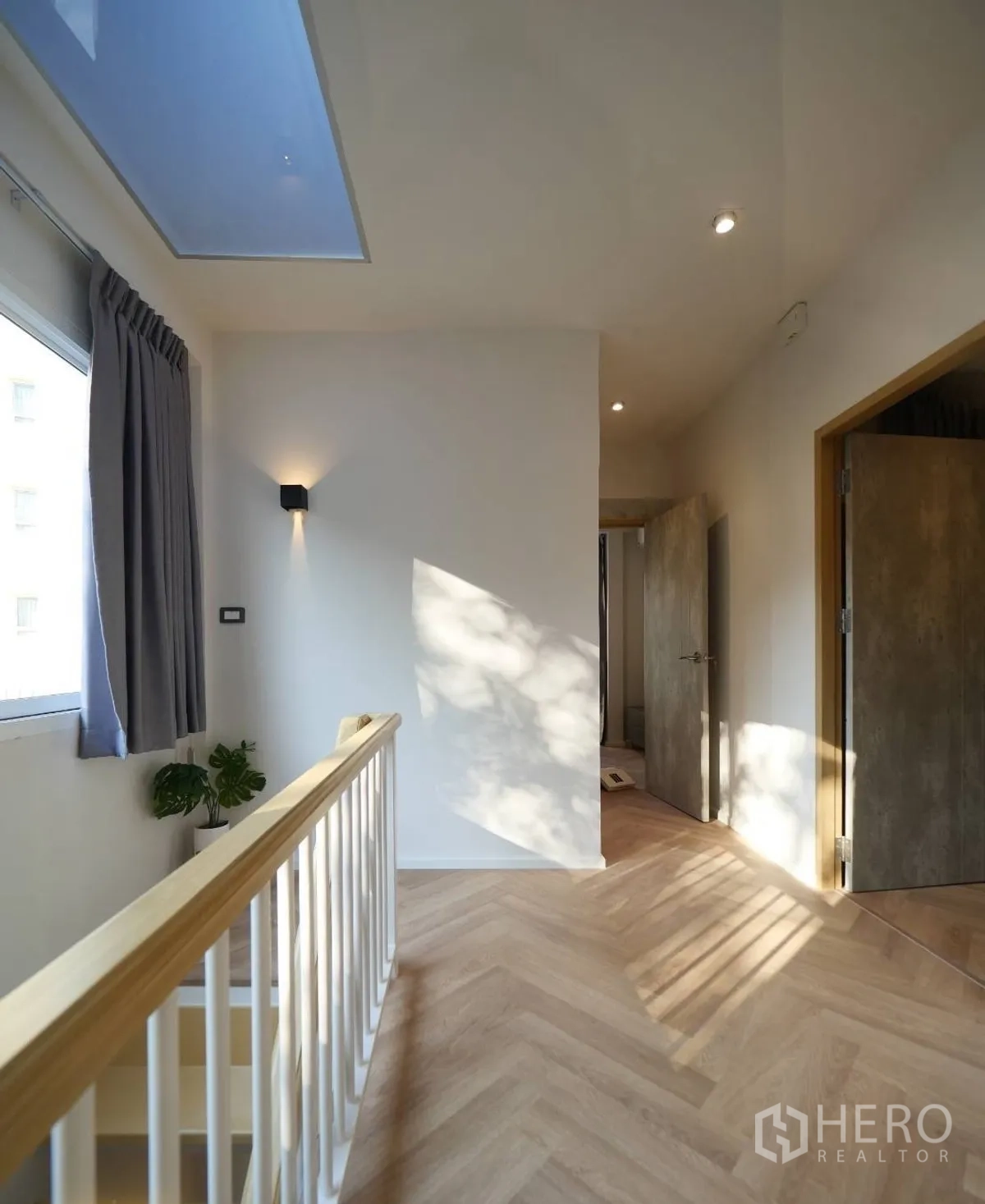 Townhouse for rent or sale in Watthana, Bangkok - Bright upstairs hallway with skylight, wooden handrail and herringbone flooring.