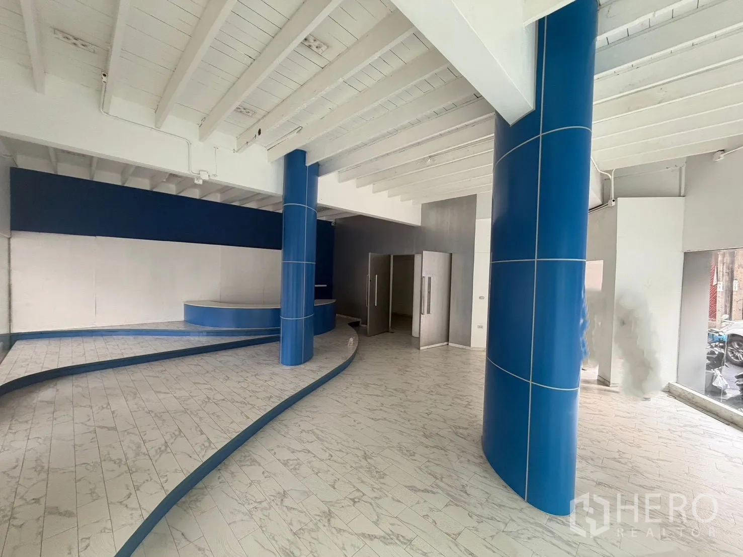 ตึกแถว for rent in Watthana, Bangkok - พื้นที่โชว์รูมกว้างมีเสาสีน้ำเงินและแท่นแสดงสินค้าทรงโค้ง.