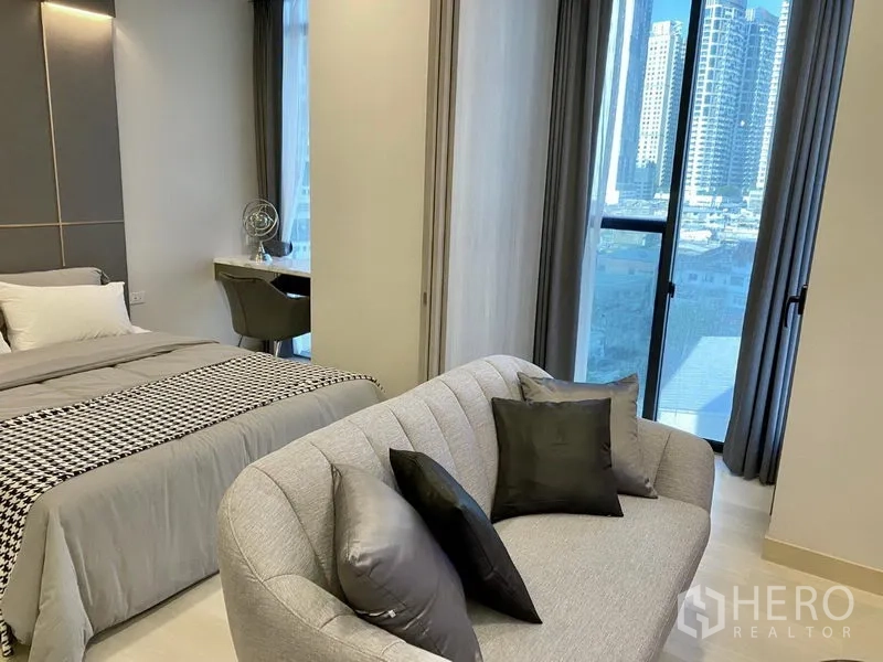 公寓 出租在Khlong Toei, Bangkok - 卧室与起居区相连，设沙发、书桌及落地窗，可见城市天际线。