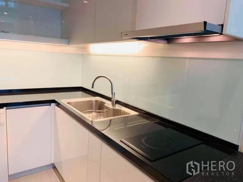 Condominium for rent in Khlong Toei, Bangkok - Modern L-shaped kitchen featuring induction cooktop, range hood, glossy cabinets and double sink.