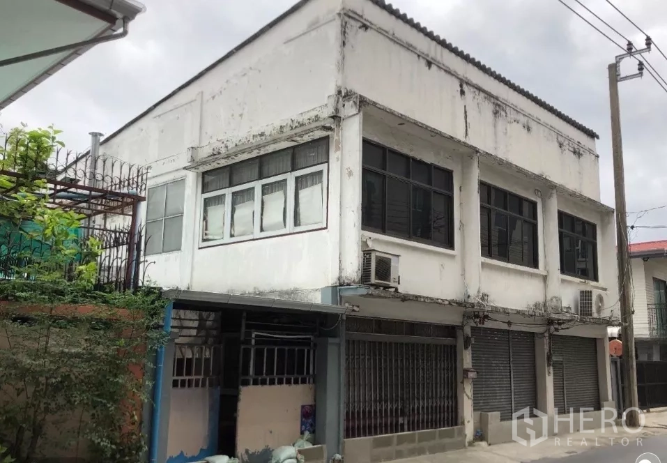 地 出售在Phra Khanong, Bangkok - 老旧两层建筑正面，卷闸与大窗户清晰，显示土地再开发潜力。