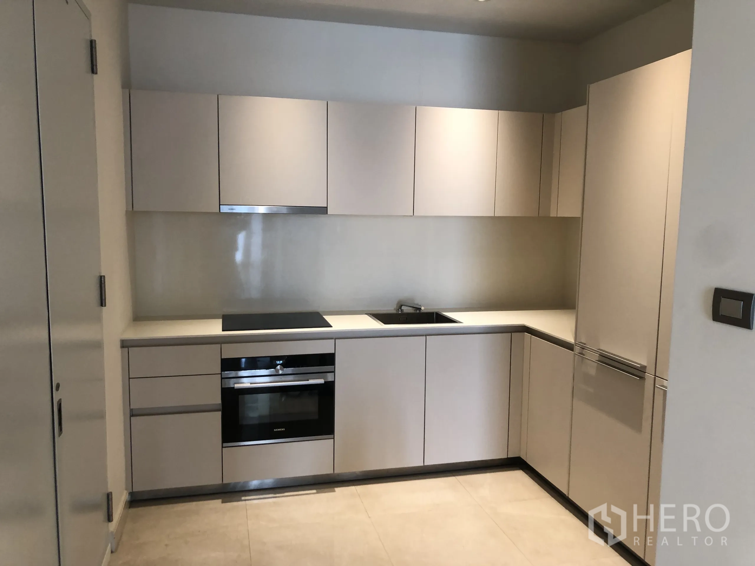 Condominium for rent in Pathum Wan, Bangkok - Contemporary L-shaped kitchen with integrated appliances, electric cooktop, oven and concealed refrigerator.