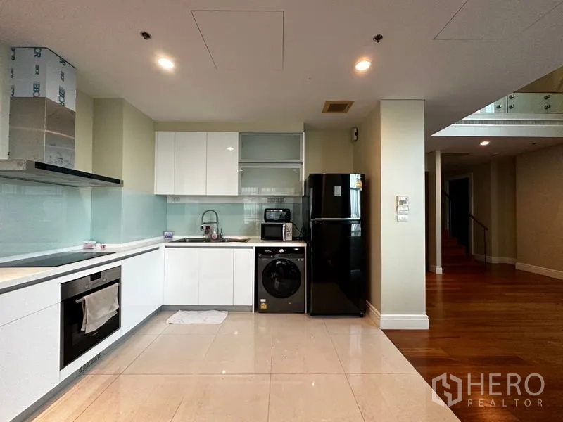 Condominium for rent in Khlong Toei, Bangkok - Sleek white kitchen with oven, cooktop, washing machine and black fridge.