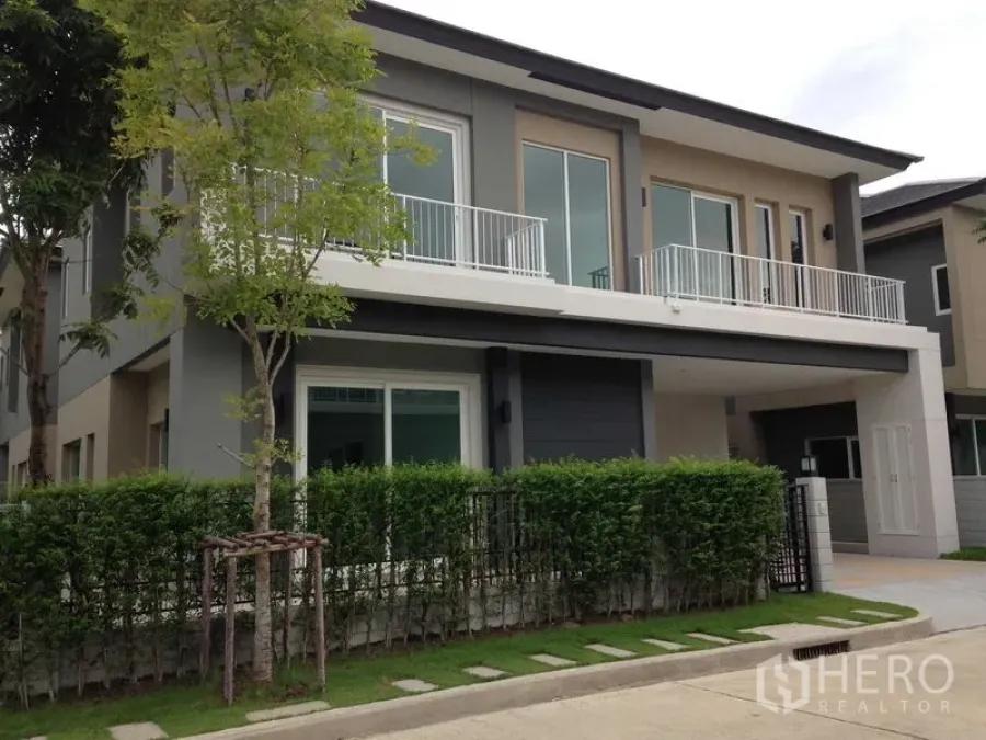 Detached House for rent or sale in Bang Na, Bangkok - Modern two-storey detached house exterior with balcony railings, hedge fence and covered carport.