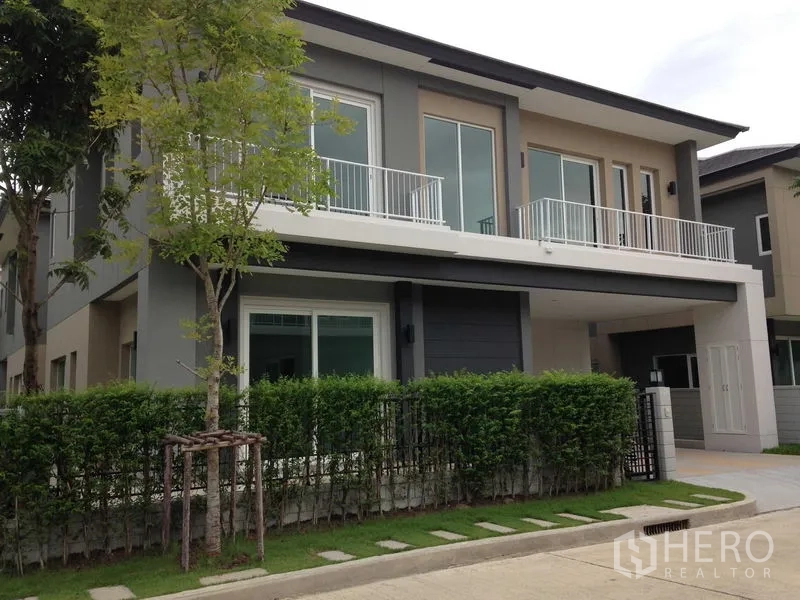 Detached House for rent or sale in Bang Na, Bangkok - Modern two-storey detached house exterior with balcony railings, hedge fence and covered carport.