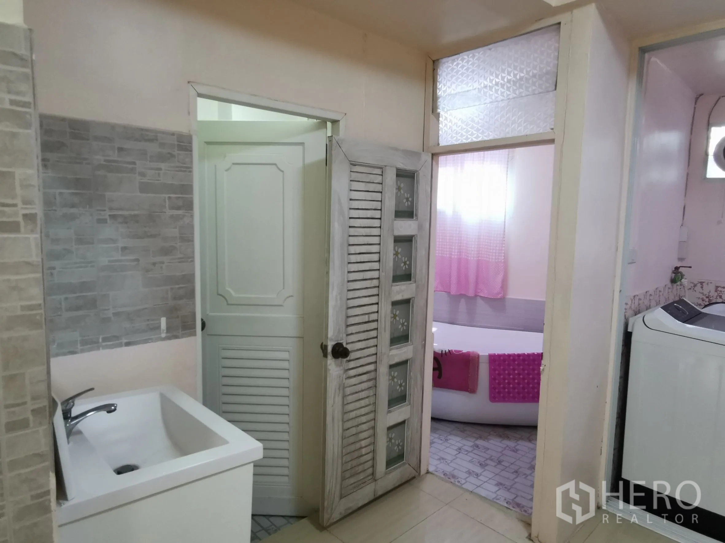 Townhouse for rent in Khlong Toei, Bangkok - Utility zone with sink, washing machine, and access to a bathroom with frosted windows.