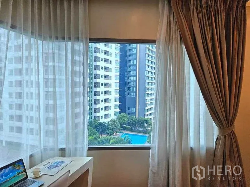 Condominium for rent or sale in Khlong Toei, Bangkok - Bedroom desk facing a large window with city towers and swimming pool view.