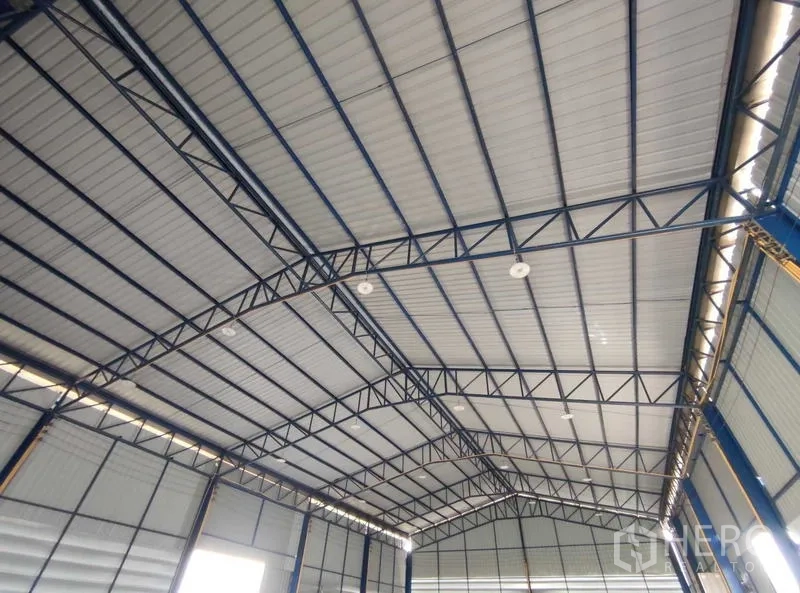Warehouse for sale in Nakhon Pathom - Interior view of the warehouse’s high arched steel‑truss roof with insulated metal panels and natural light strips.