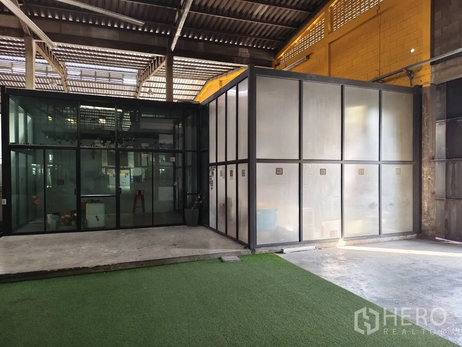 Warehouse for rent in Khlong Toei, Bangkok - Glass-enclosed office boxes beside an artificial turf zone under a high roof.