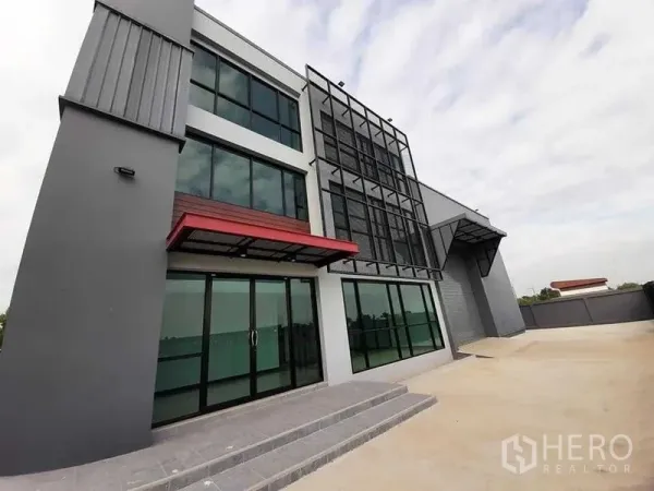Factory for rent or sale - Modern three-storey factory and office exterior with glass facade, red canopy and a wide forecourt in Lam Luk Ka, Pathum Thani.