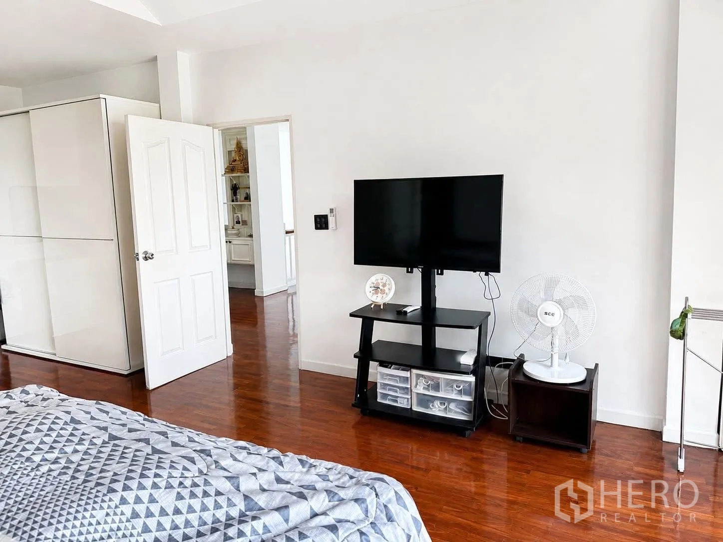 Detached House for rent in Prawet, Bangkok - Bedroom TV area with flat-screen on a stand, wardrobe, standing fan, and wooden floor.