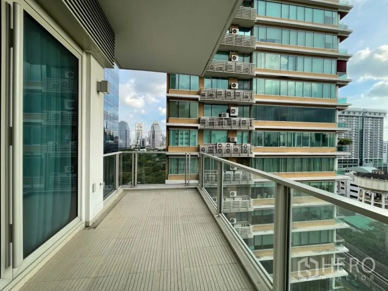 Condominium for rent or sale in Pathum Wan, Bangkok - Covered corner balcony with glass balustrade facing a neighboring modern high-rise and green views.