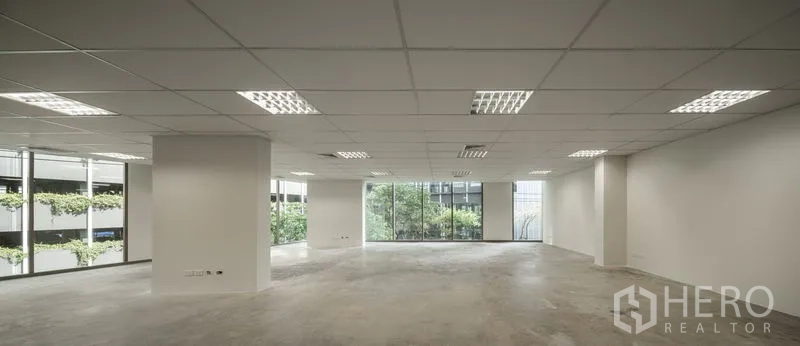 Office Space for rent in Bang Kapi, Bangkok - Open office space with big windows facing greenery and a neighboring building.