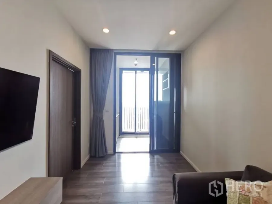 Condominium for sale in Phra Khanong, Bangkok - Living area leading to glass doors and balcony, recessed lighting and dark wood floors.