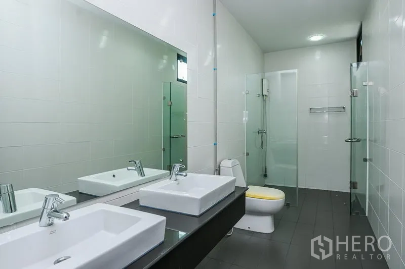 Townhouse for rent in Watthana, Bangkok - Modern bathroom with double vanity, large mirror, toilet and glass-enclosed shower.