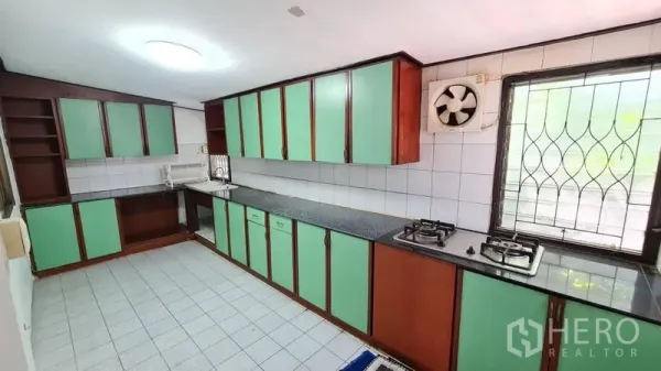 Detached House for rent in Lat Phrao, Bangkok - Separate Thai kitchen with mint-green cabinets, gas hob, tiled walls and a window with security bars.