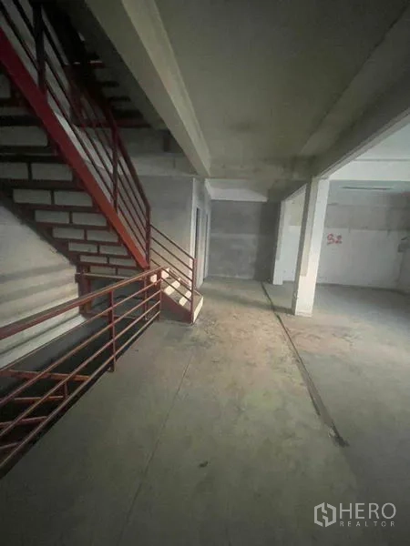 Shophouse for rent in Watthana, Bangkok - Interior with red metal staircase and unfinished concrete walls in the shophouse.