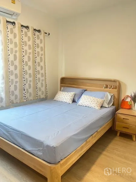 Townhouse for rent in Prawet, Bangkok - Bright bedroom with wooden bed frame, bedside table, air conditioning, and curtained window.