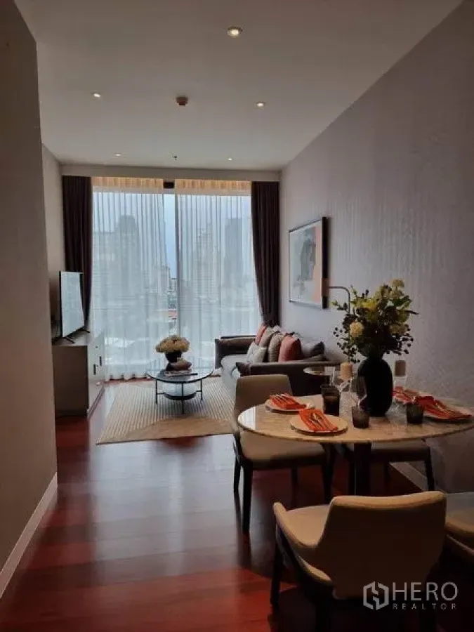 Condominium for rent in Watthana, Bangkok - Long view of dining and lounge space with artwork, set table, sofa and tall windows overlooking Bangkok.