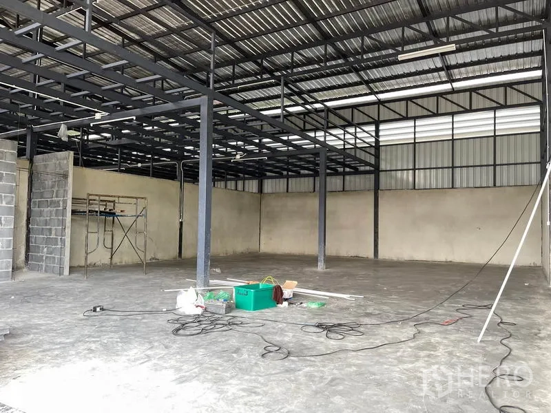 Warehouse for rent in Pathum Thani - Wide interior view of open-span warehouse under a metal roof with skylight panels.