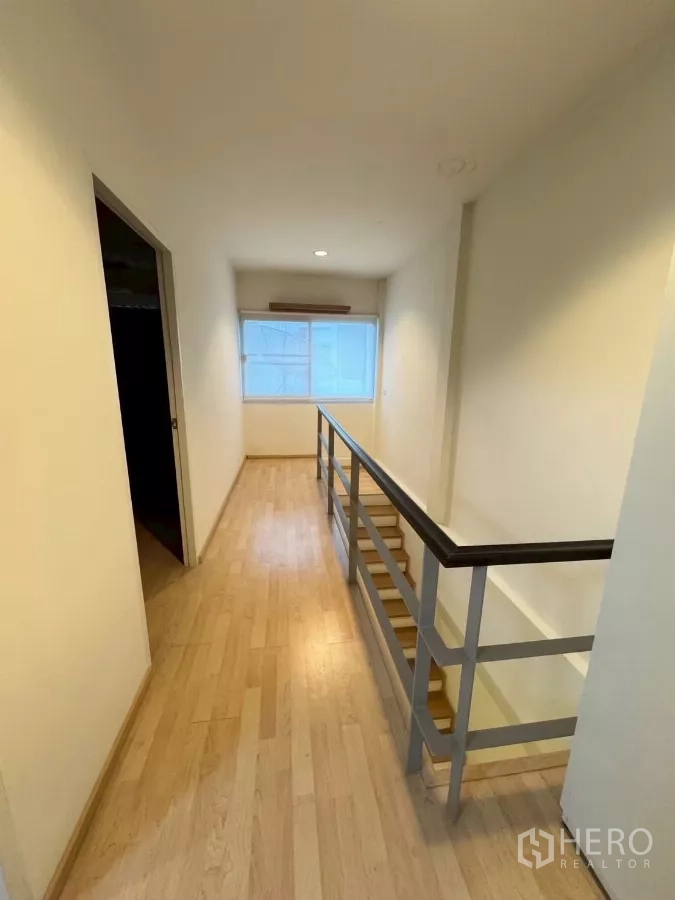 Townhouse for rent in Suan Luang, Bangkok - Upper floor corridor with wood flooring, metal handrail and window light.