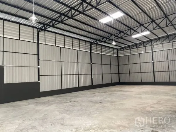 Warehouse for rent in Wang Thonglang, Bangkok - Open warehouse bay showing metal panel walls, hanging industrial lights and wide column-free space.