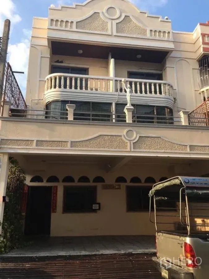 Home Office for rent in Bang Na, Bangkok - Three-storey home office facade in Bang Na with covered carport, curved balcony railings, and a beige exterior on an urban street.