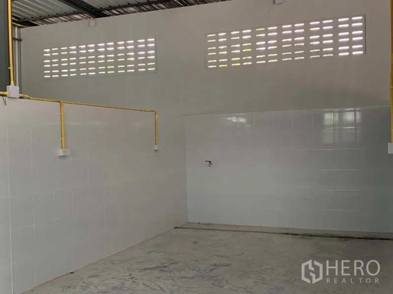 Warehouse for rent or sale in Thanyaburi, Pathum Thani - Warehouse corner showing electrical conduit, tiled surfaces and ventilated wall.